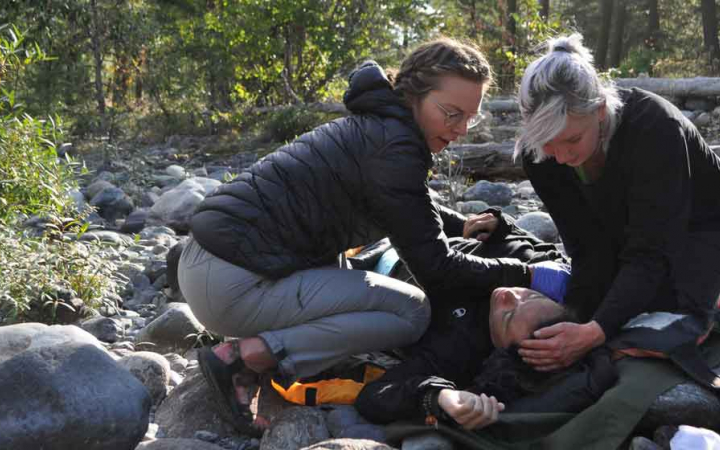 a student lays on the ground while two others tend to him during a wilderness first aid training